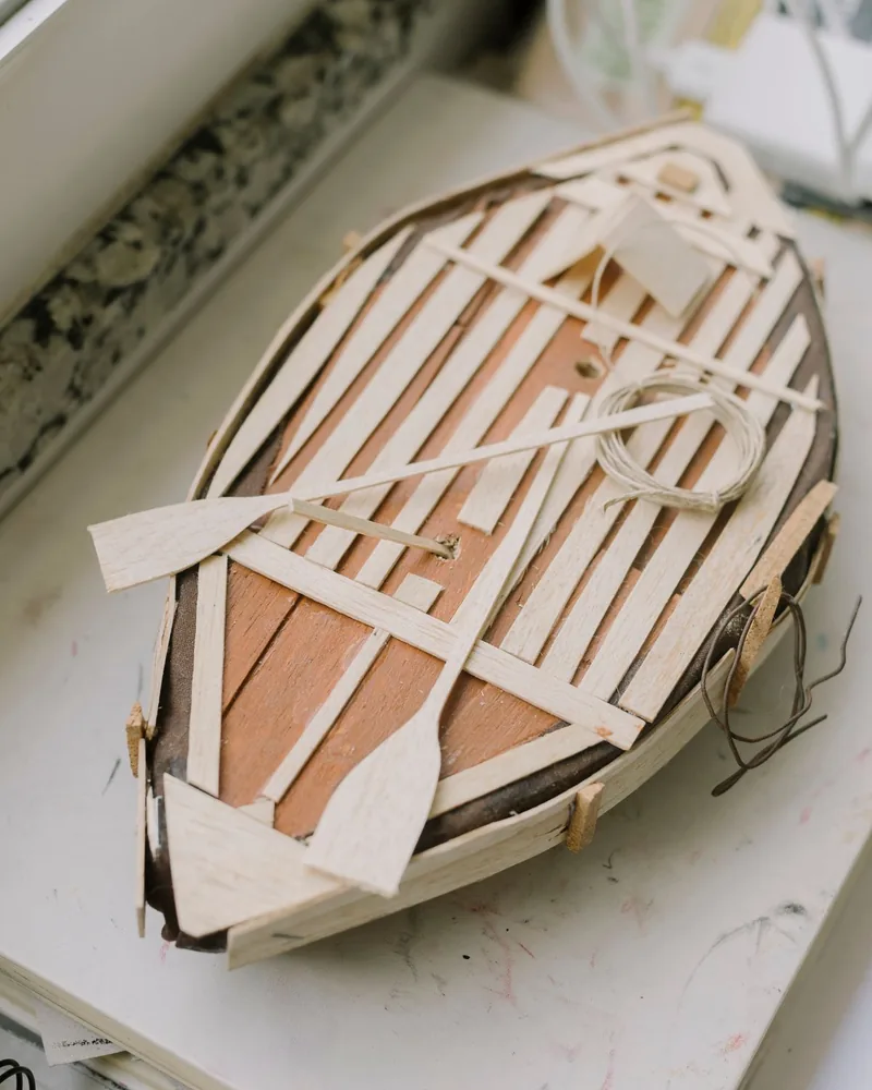 Casco de madera de un modelo de barco en construcción sobre el banco de trabajo, rodeado de herramientas de modelismo
